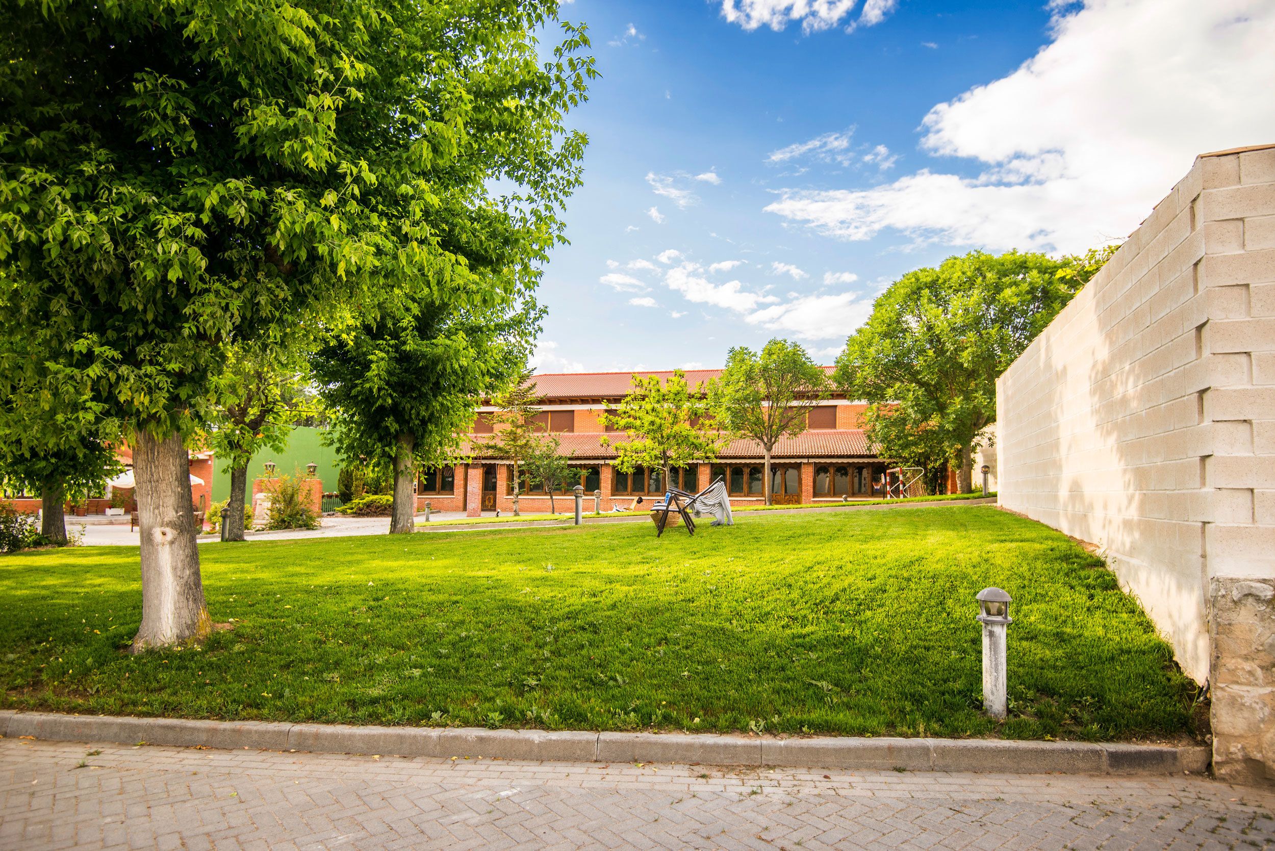Un patio con un edificio de ladrillo, césped verde y árboles.