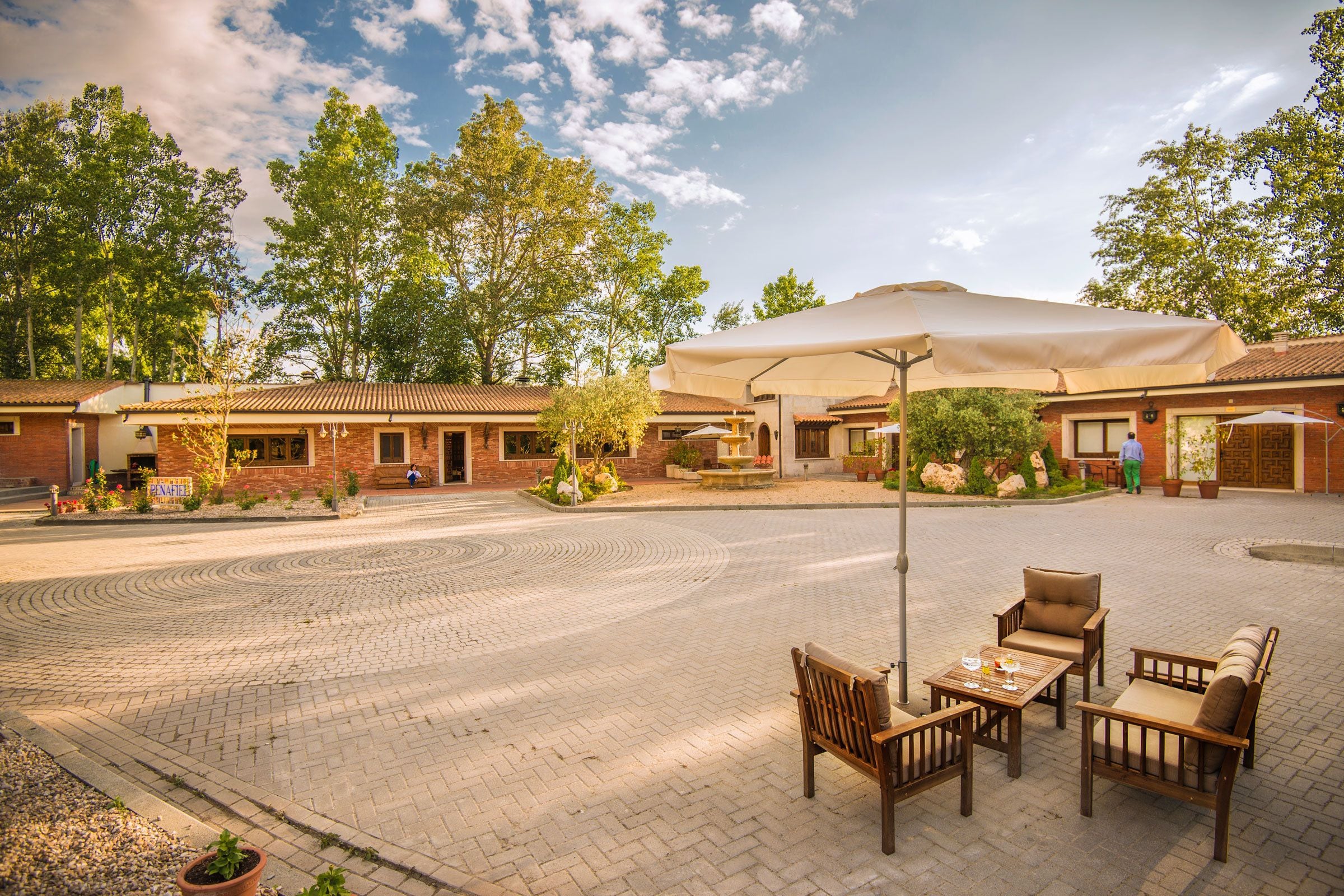 A courtyard with outdoor seating, a fountain, and a building with a tiled roof.