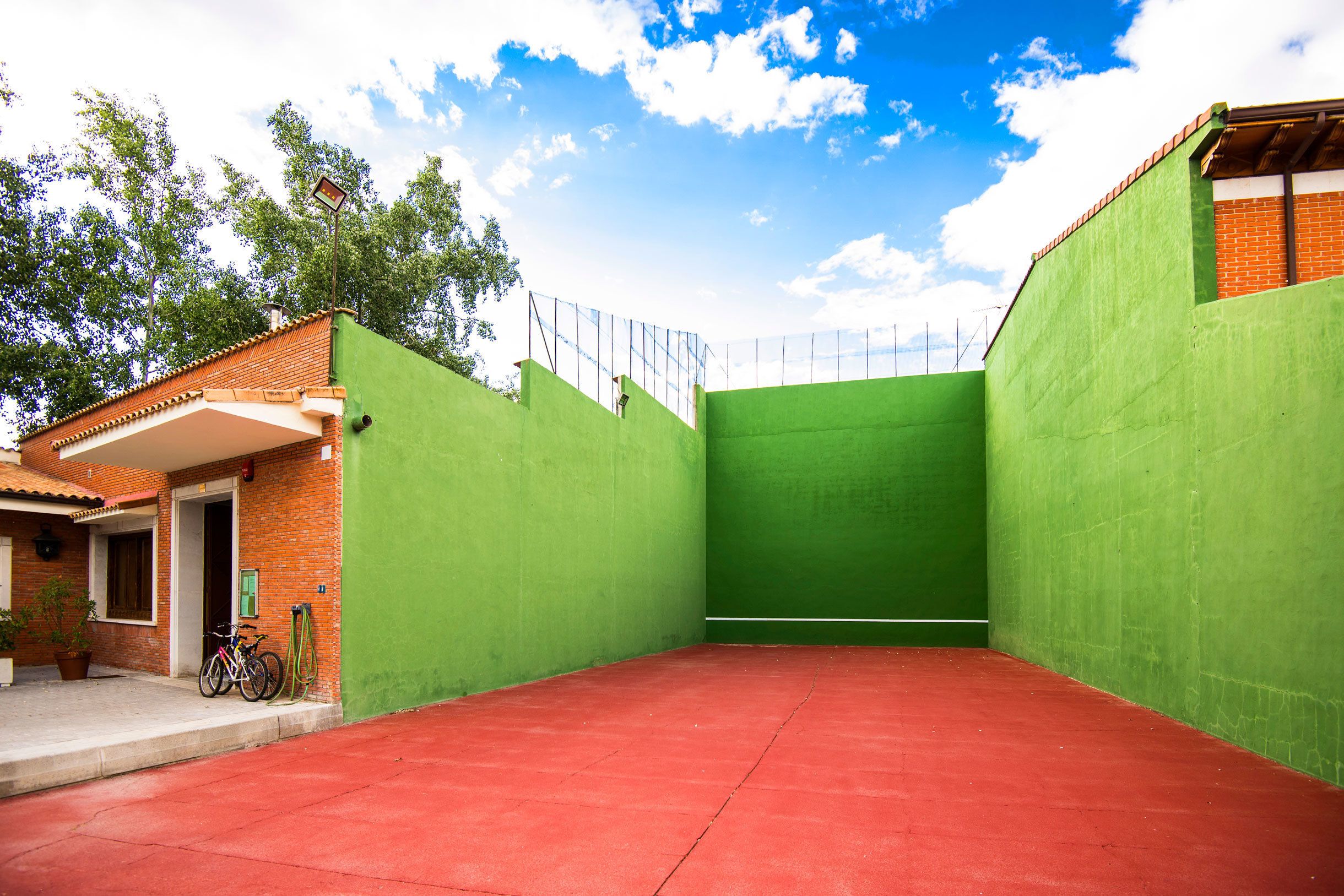 A courtyard with a red floor, green walls, and a brick building with a door and windows.