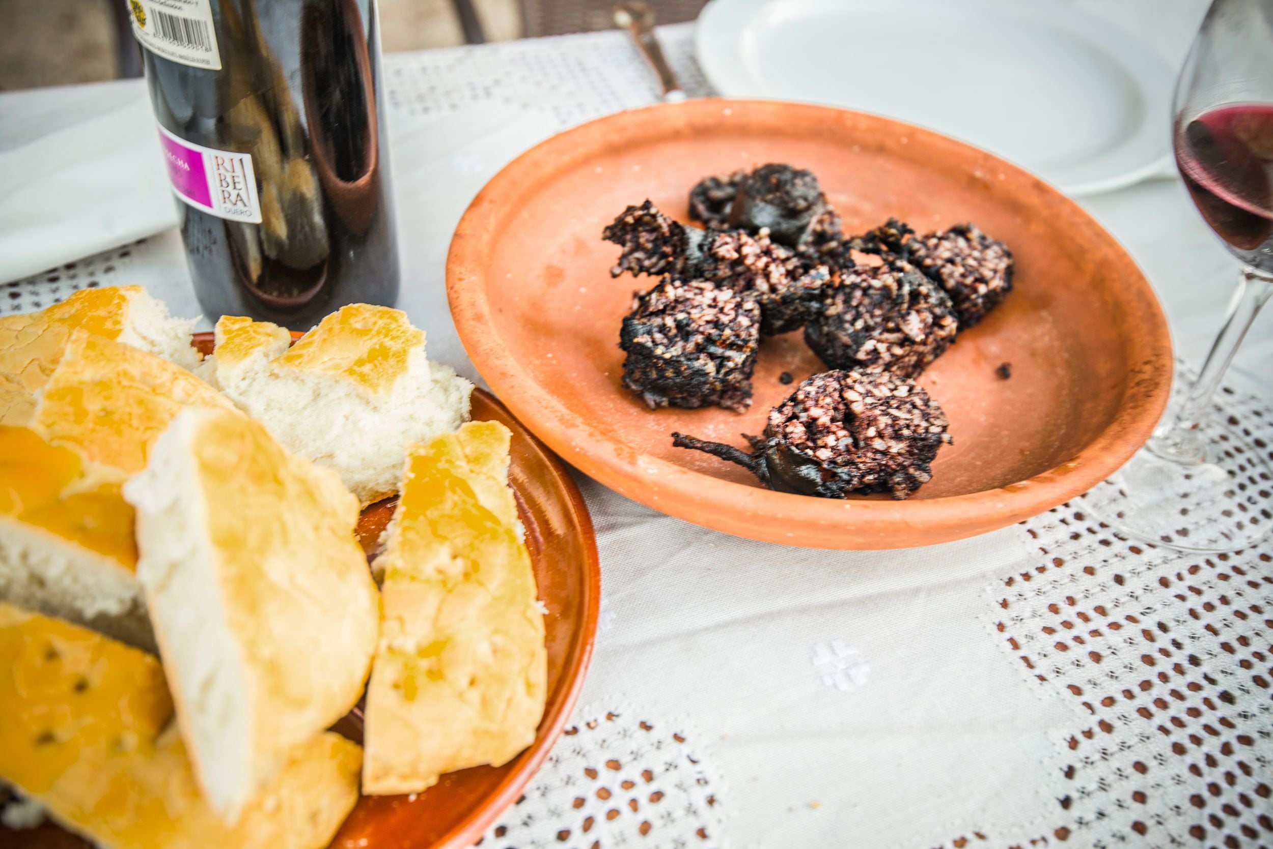 Uma mesa com um prato de terracota segurando pão e uma garrafa de vinho.