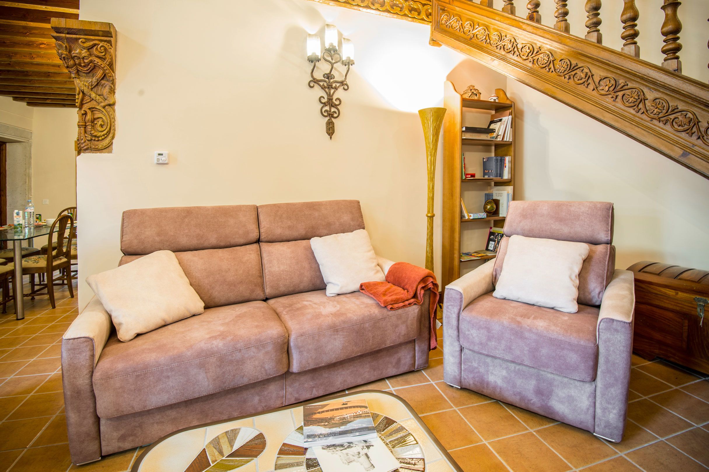 Una sala de estar con sofá y sillón, una lámpara y una escalera con barandilla decorada.