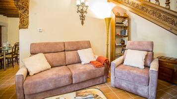 Una sala de estar con sofá y sillón, una lámpara y una escalera con barandilla decorada.