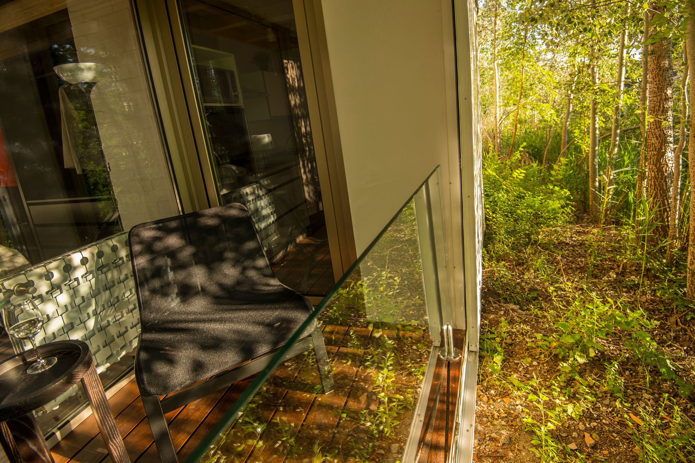 A glass table with a chair, a glass vase, and a wooden floor.