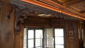A wooden interior with a decorative ceiling, a window with a view, and a door with a handle.