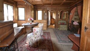 A wooden cabin interior with a round table, floral chairs, a wooden bench, and a patterned rug.