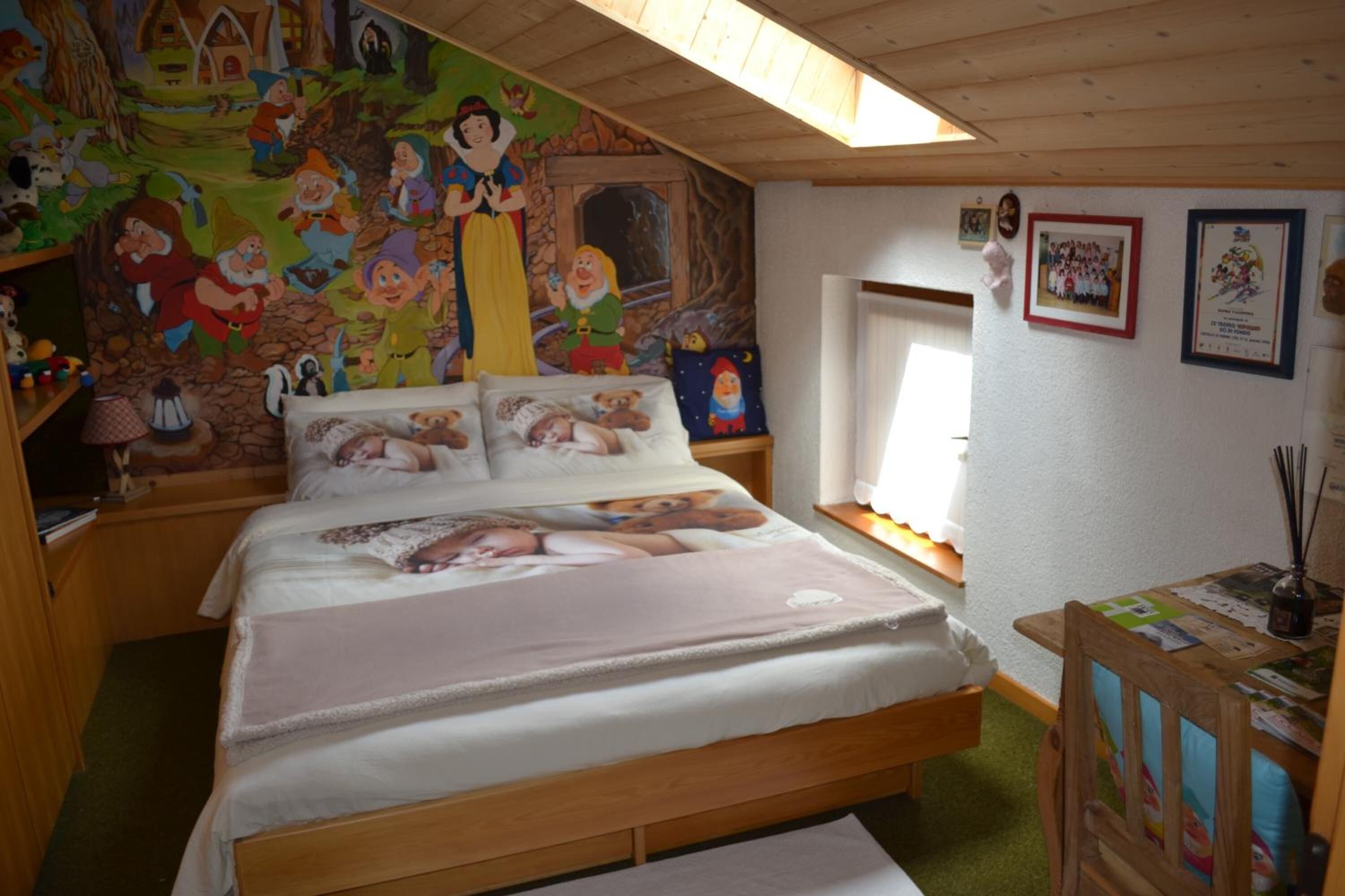 A cozy bedroom with a bed, a mural on the wall, and a window.