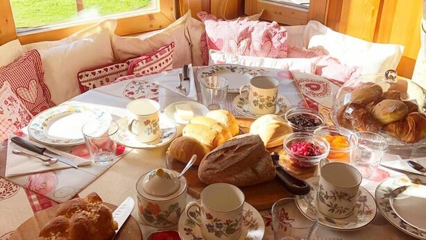 A breakfast setting with a table set for two, featuring bread, pastries, and tea cups.