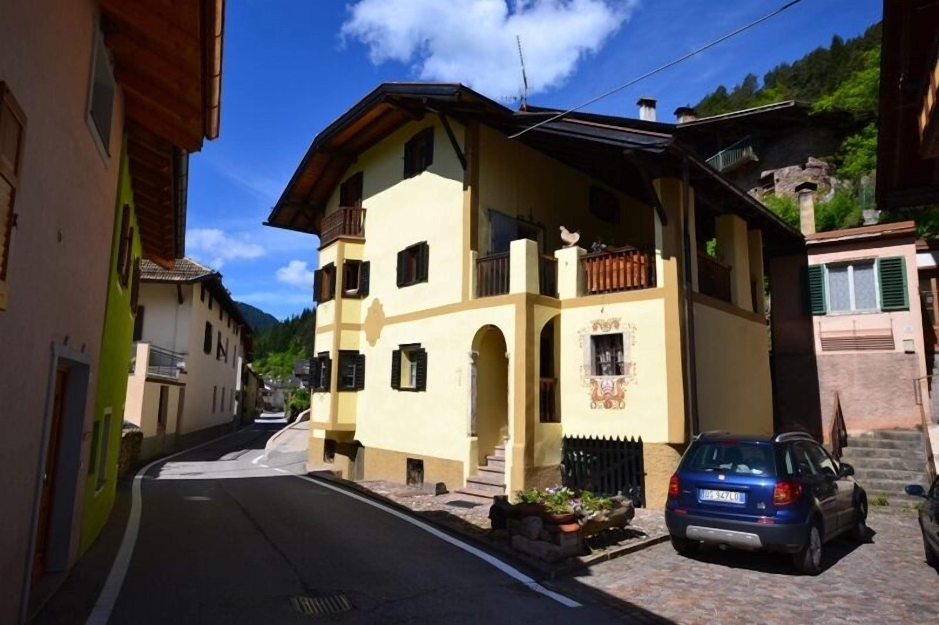 Un edificio di due piani con un balcone, un'auto parcheggiata davanti e un cielo sereno.