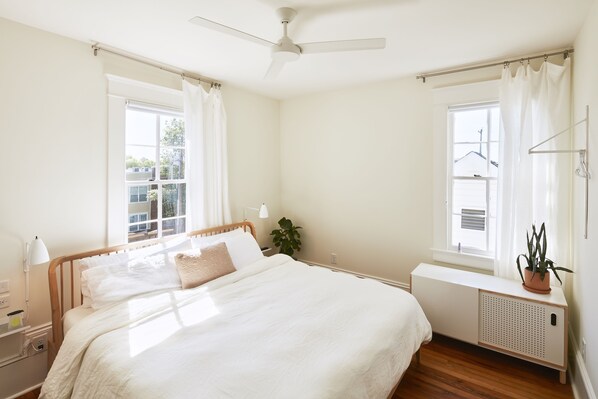 A bedroom with a bed, bedside table, lamp, window, ceiling fan, and a radiator. - Guest House Raleigh (Raleigh)