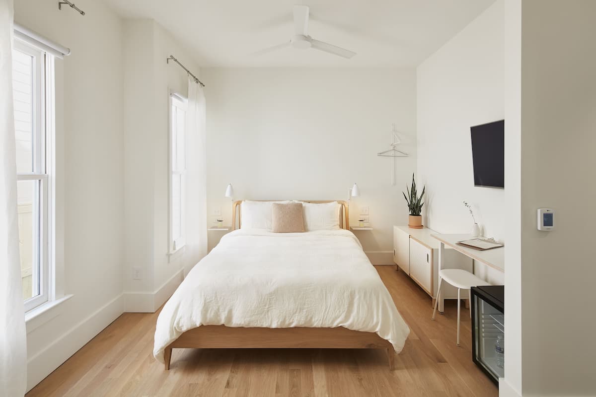A modern bedroom with a wooden bed, bedside tables, a desk, and a small seating area.