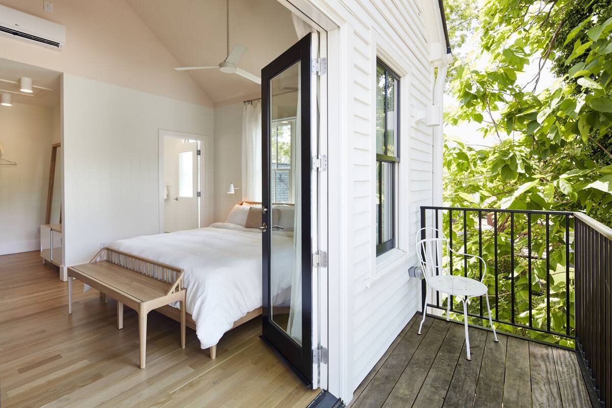 A bedroom with a bed, a wooden bench, and a sliding glass door leading to a balcony with a chair.