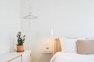 Un dormitorio con cama, mesita de noche, lámpara y un perchero.
