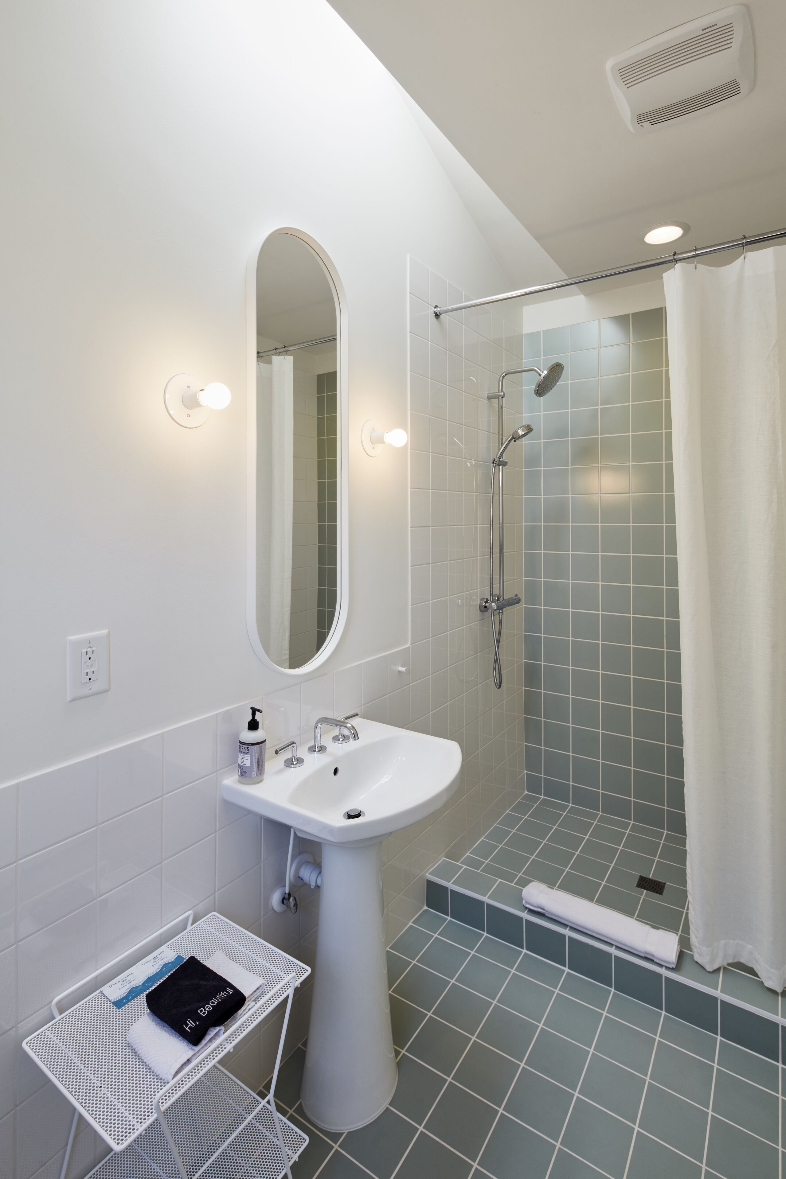 A bathroom with a sink, mirror, shower, and a towel rack.