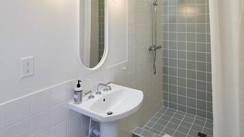 A bathroom with a sink, mirror, shower, and a towel rack.