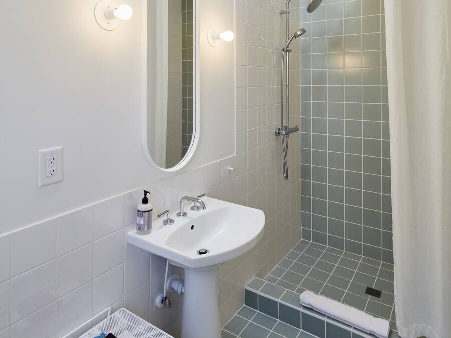 A bathroom with a sink, mirror, shower, and a towel rack.