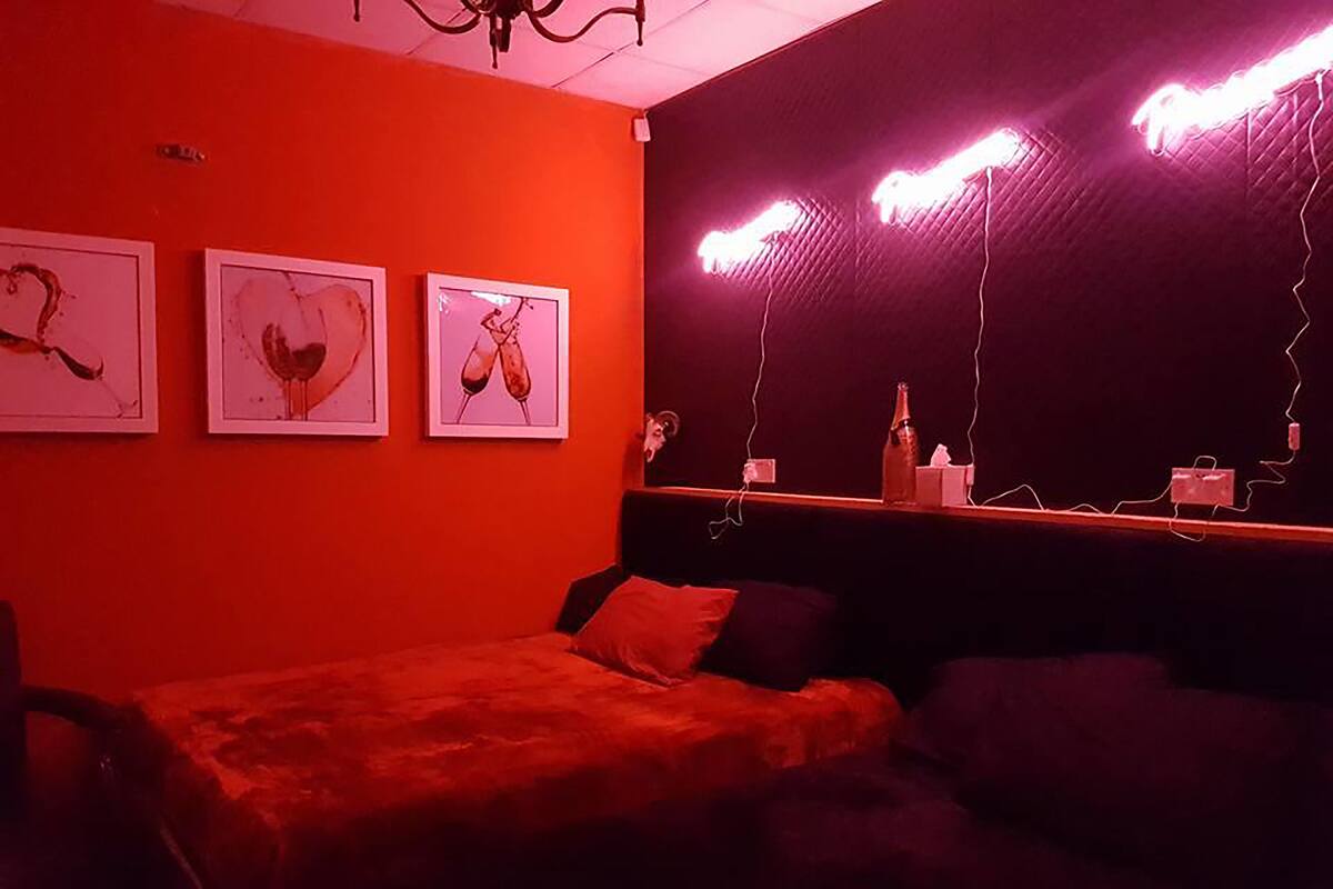 A room with a red wall, a bed, a couch, and three framed pictures.
