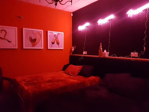 A room with a red wall, a bed, a couch, and three framed pictures.