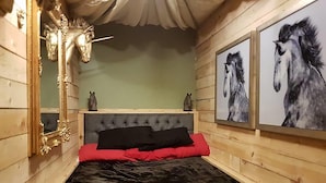 Ett sovrum med en stoppad sänggavel, en stor spegel och två inramade tavlor med hästmotiv på väggen.