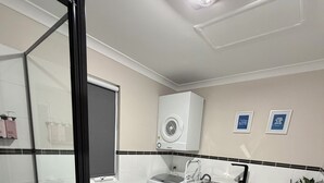 Ett modernt badrum med en duschkabin i glas, en toalett, ett handfat och en inbyggd tvättmaskin.