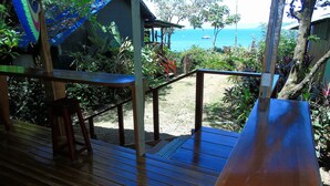 Terraza de madera con barandilla, con vista a una playa, barcos y una vista despejada del océano.