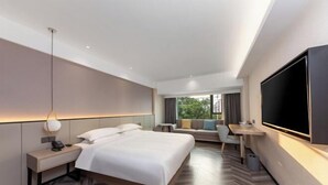Ein modernes Hotelzimmer mit einem großen Bett, einem Schreibtisch, einem Flachbildfernseher und Blick ins Freie.