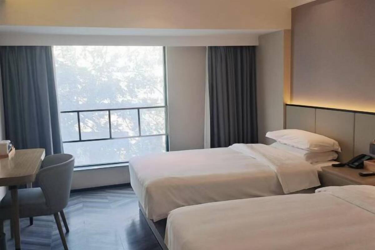 A hotel room with two beds, a desk, and a window with curtains.