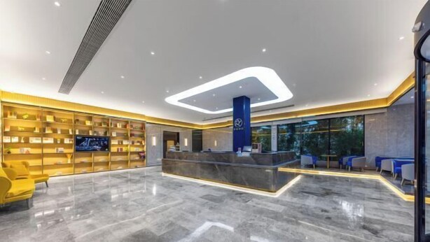 Eine moderne Hotelhalle mit Marmorboden, einer Rezeption und einer Sitzecke mit gelben Stühlen.