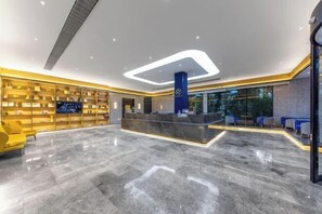 Um hall de hotel moderno com piso de mármore, balcão de recepção e área de estar com cadeiras amarelas.