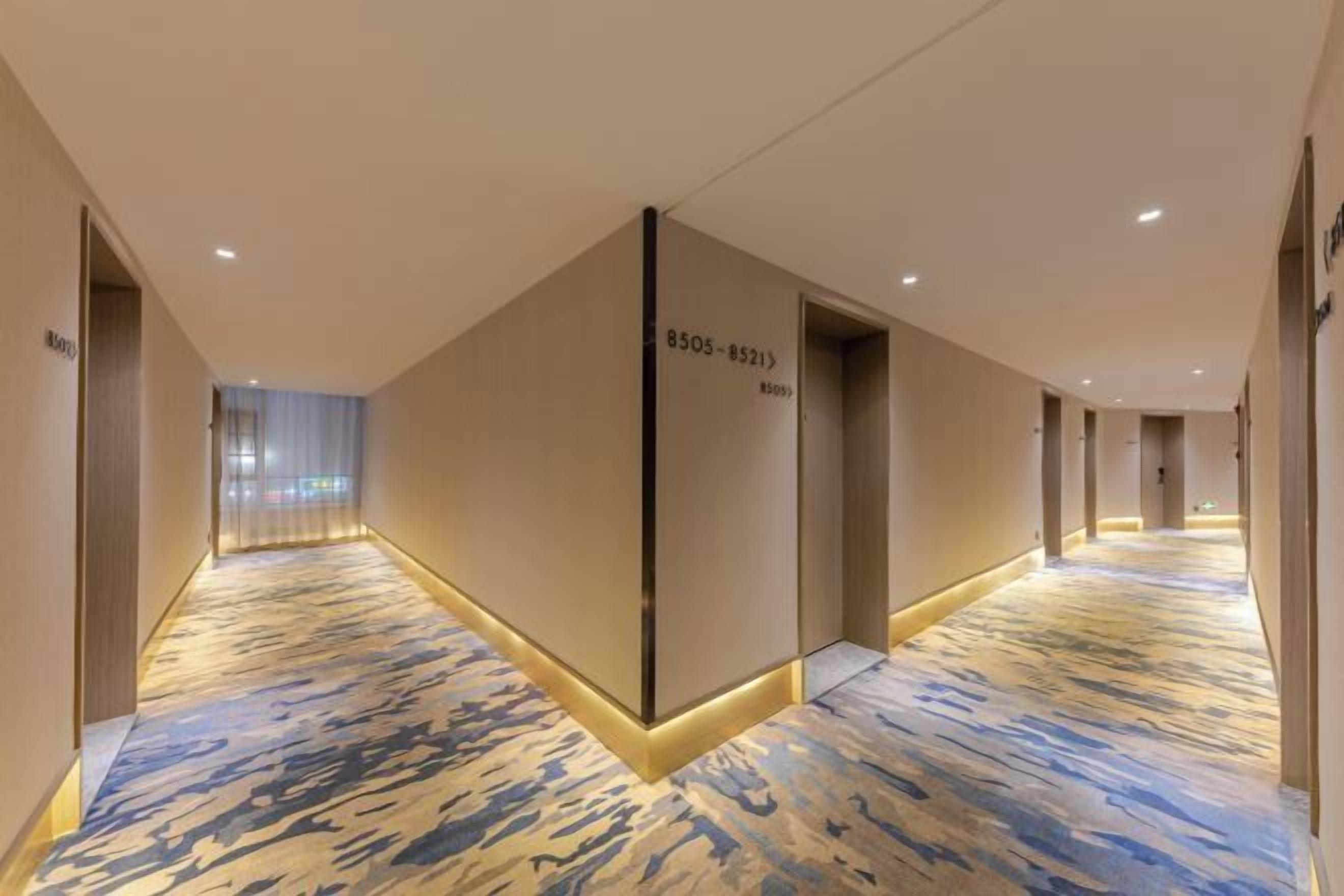 A hotel corridor with a patterned carpet, doors with room numbers, and a modern design.