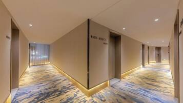 A hotel corridor with a patterned carpet, doors with room numbers, and a modern design.