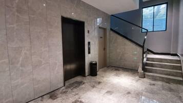 A modern elevator, a staircase, and a trash bin in a lobby area.