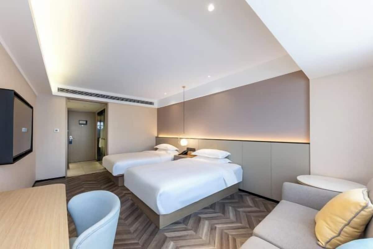A hotel room with two beds, a desk, and a sofa.