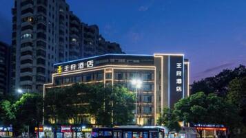 A multi-story hotel with illuminated signage, a bus stop in front, and a tall residential building in the background.