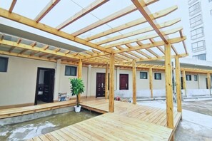 Ein überdachter Außenbereich mit einer Holz-Pergola, einem kleinen Wasserspiel und einem Topfpflanzen.
