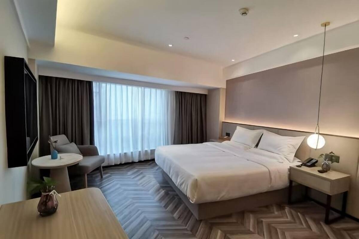 A hotel room with a bed, bedside table, lamp, chair, and a small table.