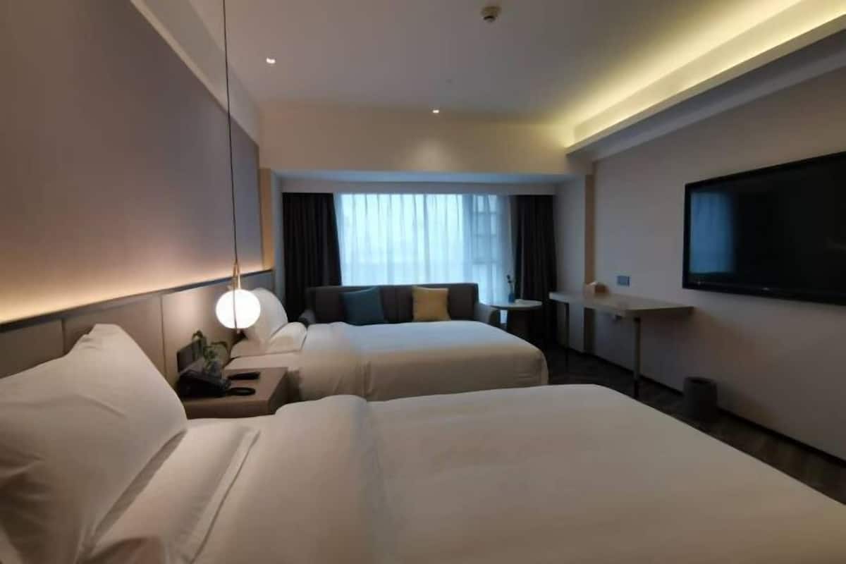 A hotel room with two beds, a TV, a desk, a lamp, and a window with curtains.