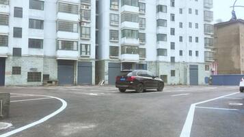 A multi-story residential building with balconies, a parked car, and a clear road.