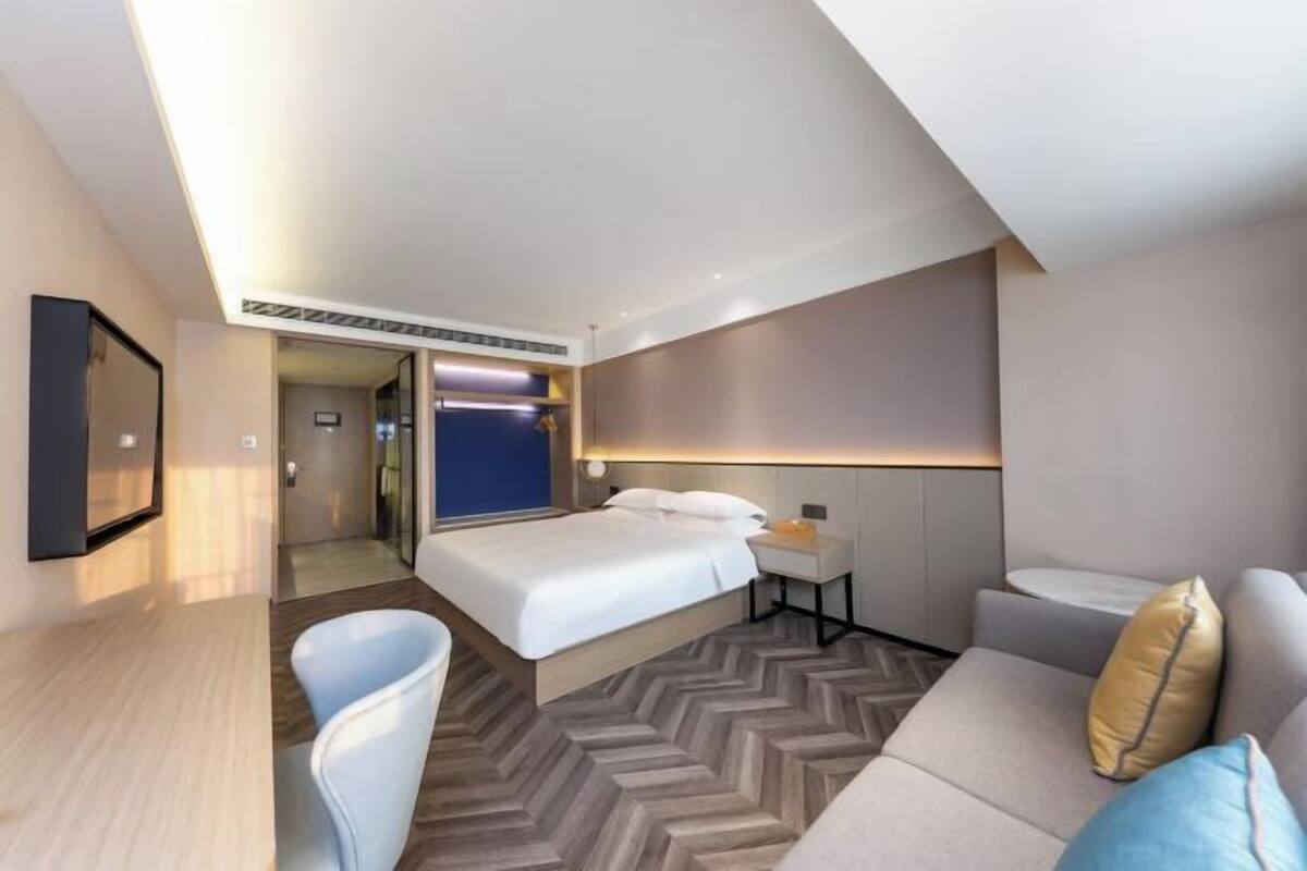A modern hotel room with a large bed, a desk, a chair, and a sofa.