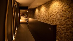 A hallway with a stone wall, a reception desk, and a seating area with chairs and a table. - Albergo Miramonti (Scanno)