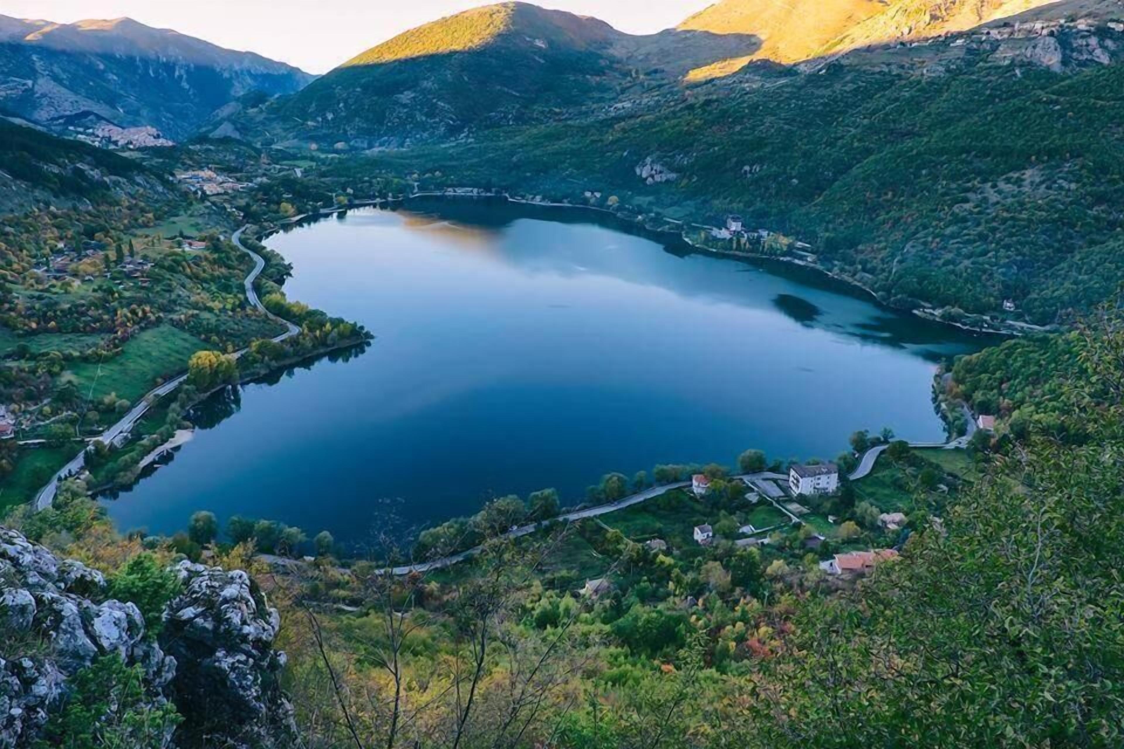 A lake surrounded by hills with a few buildings near the water's edge.