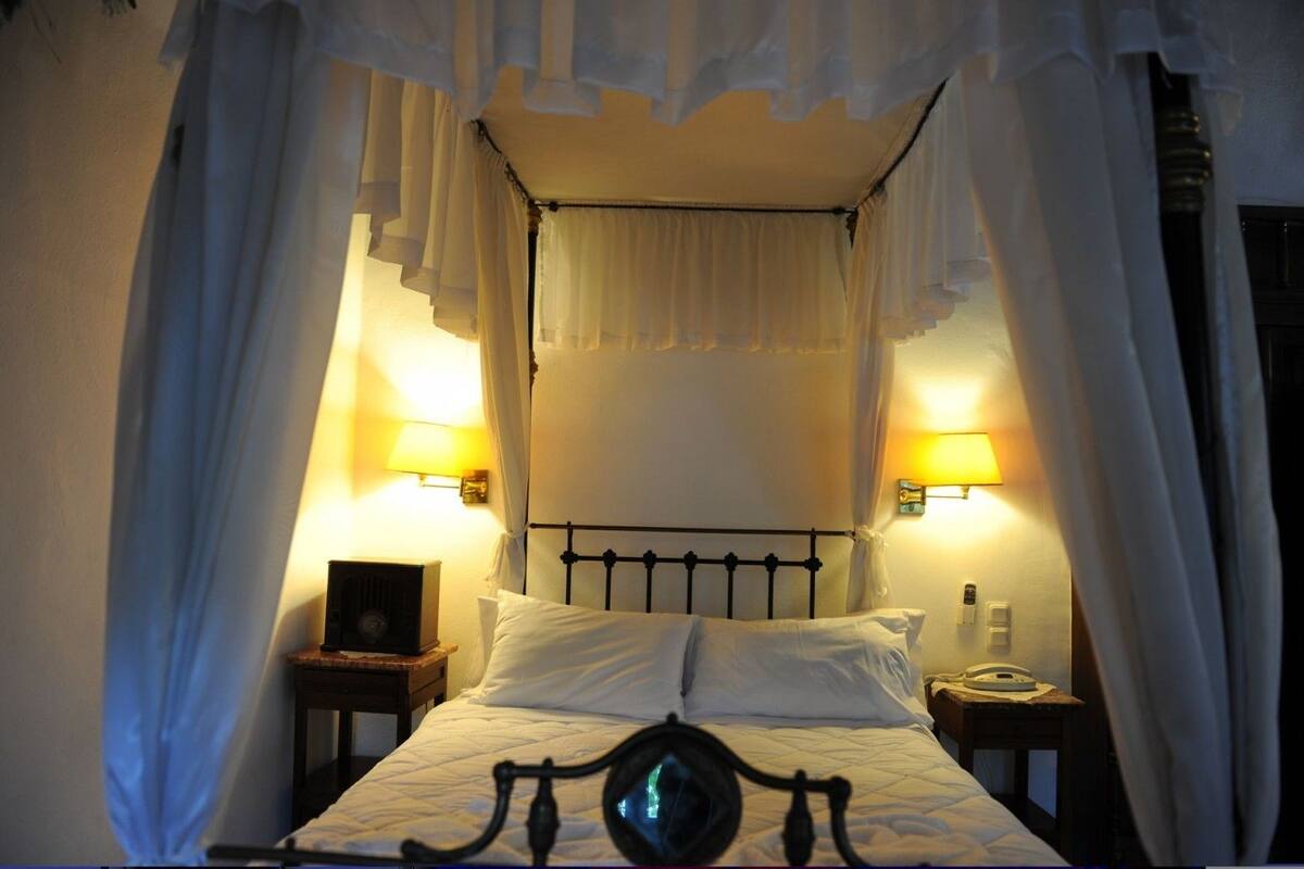 A bed with a canopy, two bedside lamps, and a nightstand with a clock.