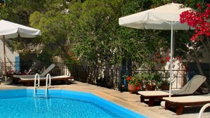 Une piscine entourée de plantes en pot et d’arbres, avec des chaises longues et des parasols à proximité.