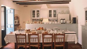 Un coin repas avec une table dressée pour quatre personnes, des chaises en bois et, au fond, une cuisine équipée d’armoires et d’appareils électroménagers.