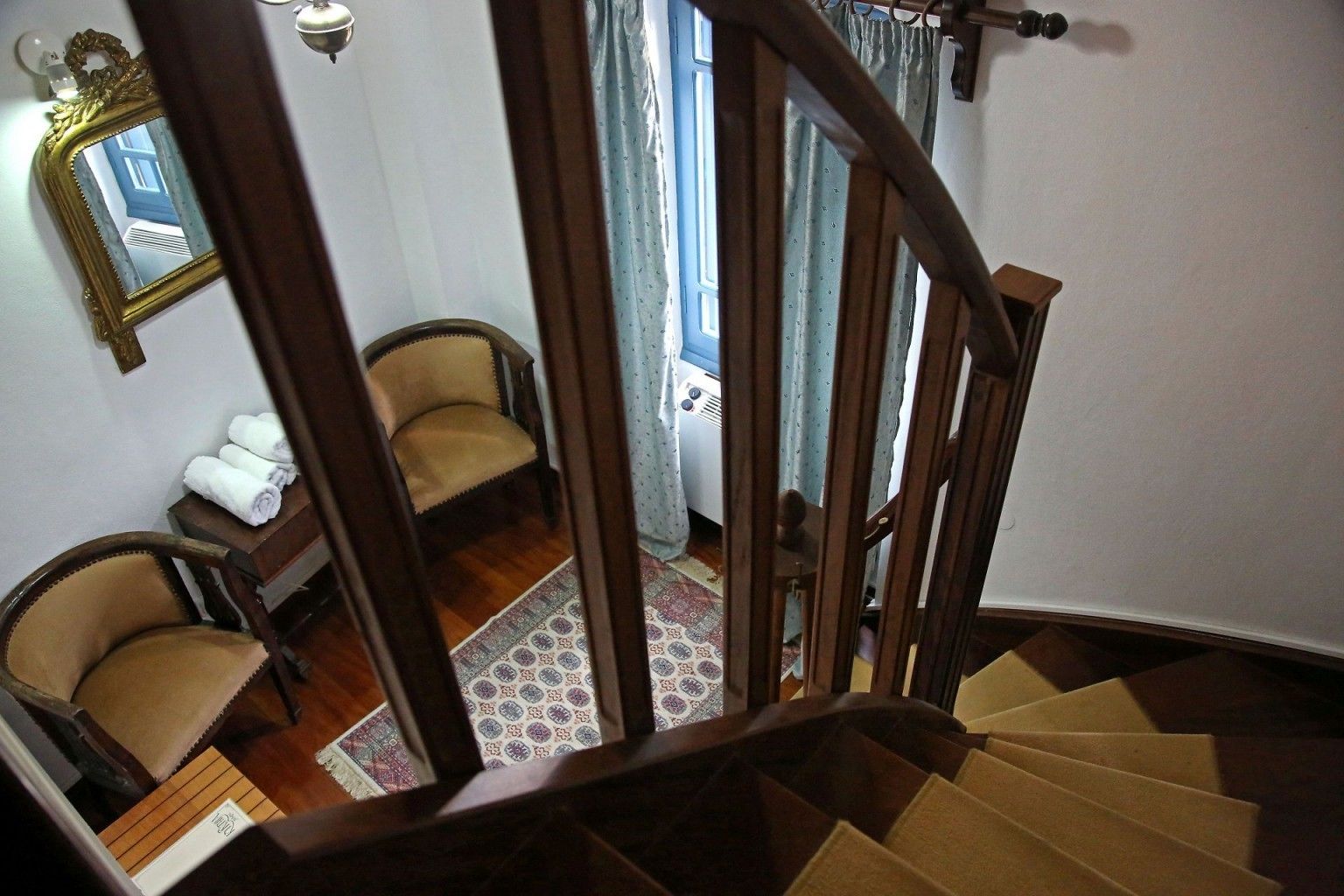 Un escalier avec des rampes en bois, un tapis à motifs et deux fauteuils avec des coussins.