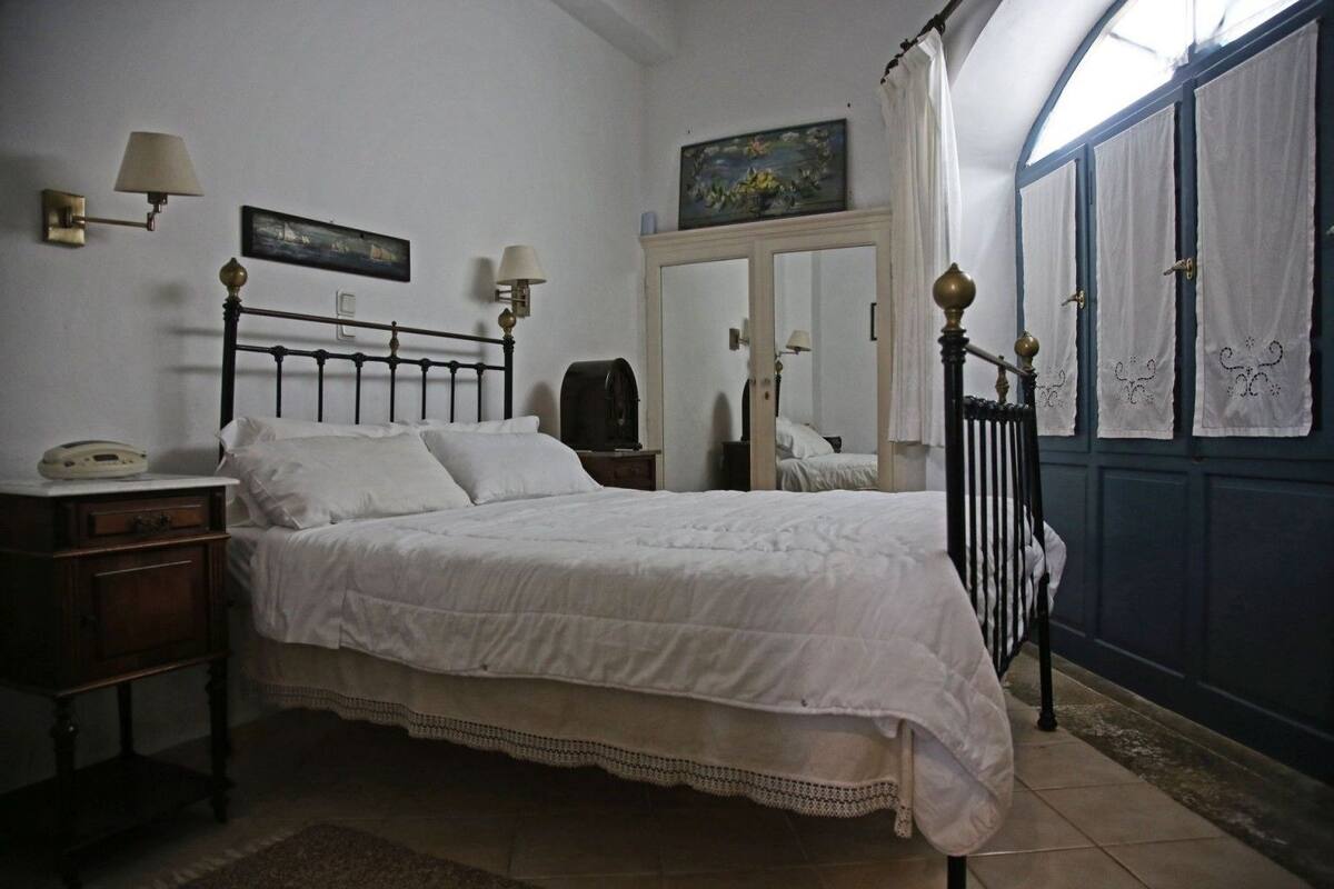 A bedroom with a single bed, a nightstand, a lamp, a mirror, and a window with curtains.