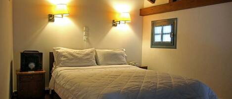 A bedroom with a bed, two wall-mounted lamps, a nightstand with a telephone, and a window with curtains.