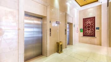 A hotel lobby with elevators, a reception desk, and a decorative wall piece.