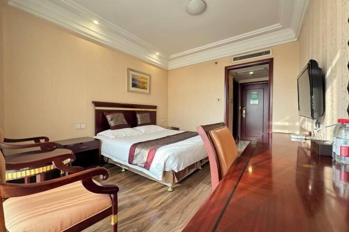 A hotel room with a bed, wooden furniture, a television, and a door leading to another room.
