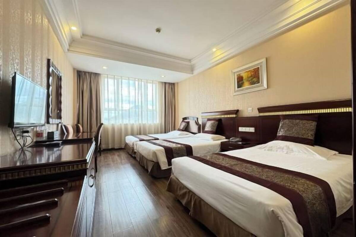 A hotel room with two beds, a desk, a television, and a window with curtains.