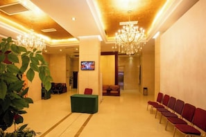 Een hotel lobby met een receptiebalie, een zithoek en een televisiescherm.